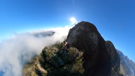a young and strong solo hiker is walking along the steep edge of espigao amorelo in madeira with thin clouds around him as he takes a dangerous step up to a rock on the cliffside to enjoy the view.