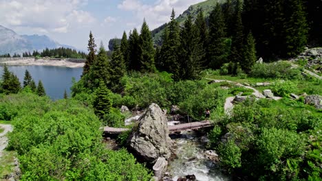 Young-woman-strolling-over-bridge-across-stream-in-picturesque-alp-setting,-Switzerland