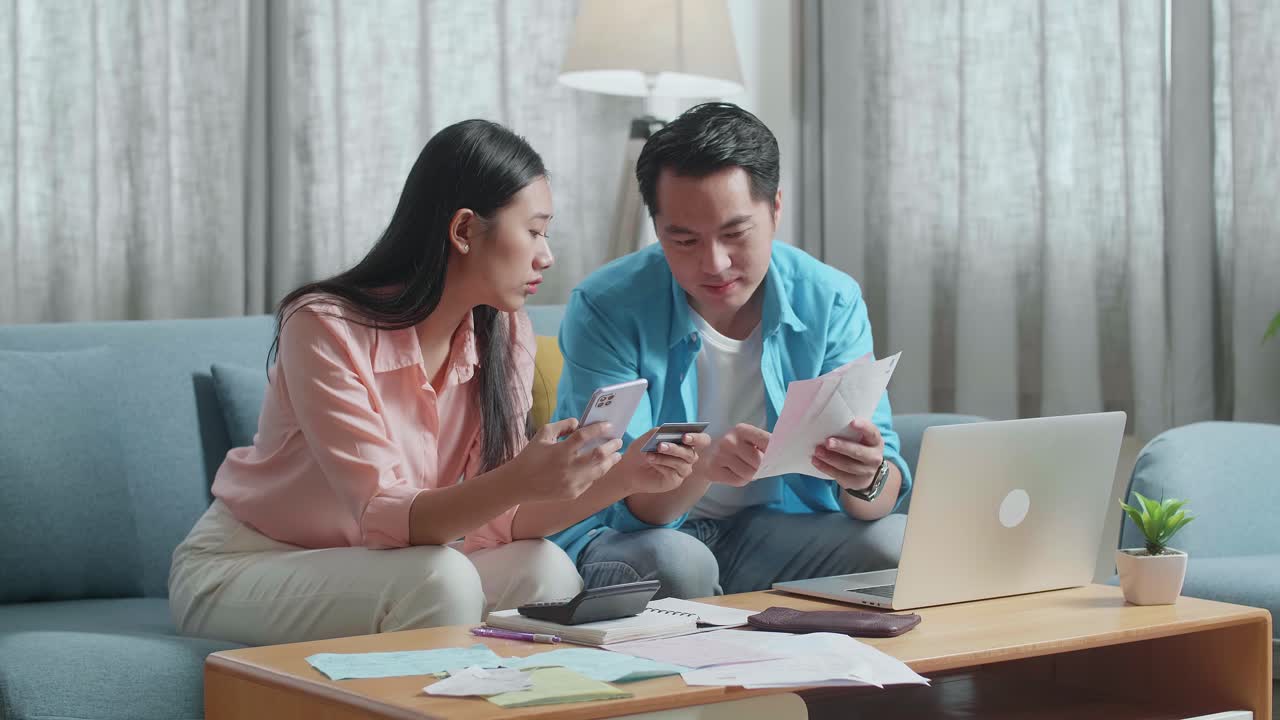 Asian Couple With A Laptop Holding Credit Card And Smartphone Having Headache Due To Unable Pay Money