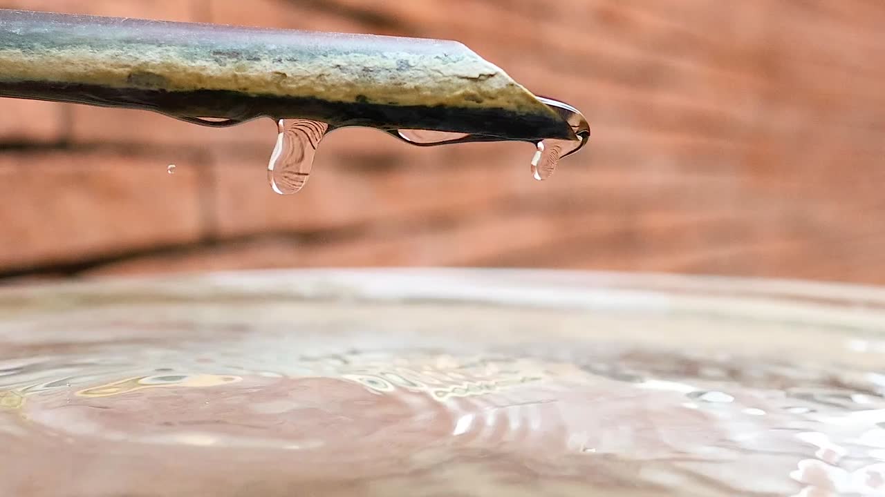 Gocce d'acqua al rallentatore che cadono da un tubo, creando increspature in una vasca di pietra.