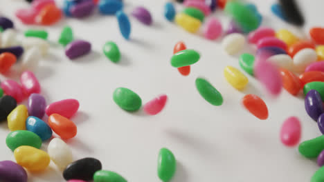 Video-of-close-up-of-multi-coloured-sweets-falling-over-white-background