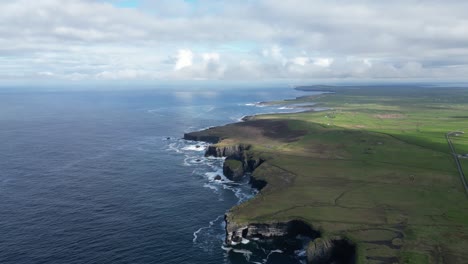 rugged coastline with waves crashing on cliffs, green fields alongside the ocean, drone footage