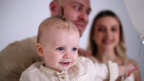 happy little baby holding a balloon. loving parents at backdrop in blur. family portrait in studio.