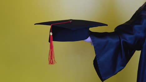 master's hat with a red tassel on the hand of a university graduate. close up view on a yellow background