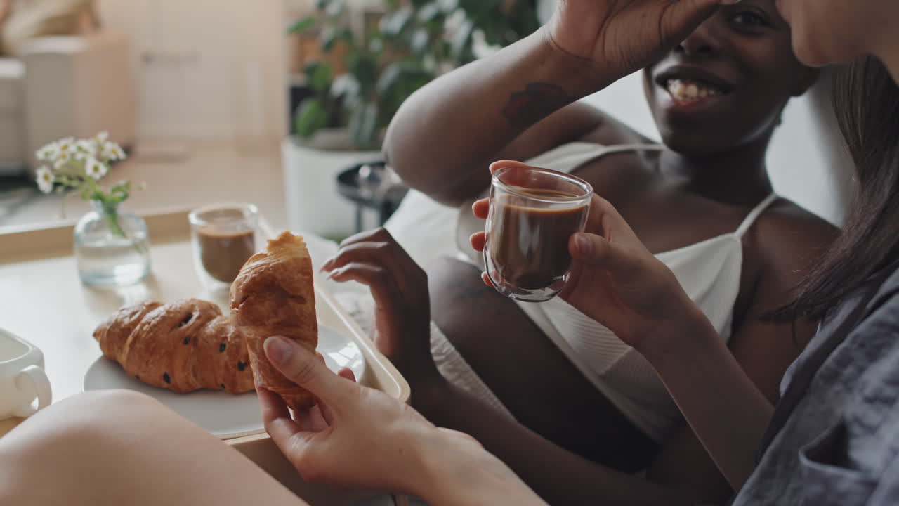 Happy Woman Sharing Croissant with Girlfriend in Bed