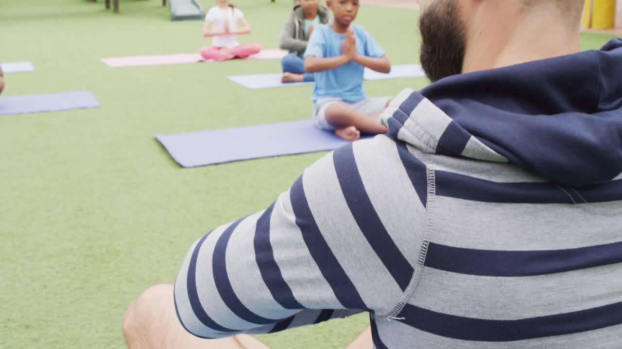 un maestro masculino diverso y escolares felices haciendo ejercicio en esteras en el patio de recreo de la escuela