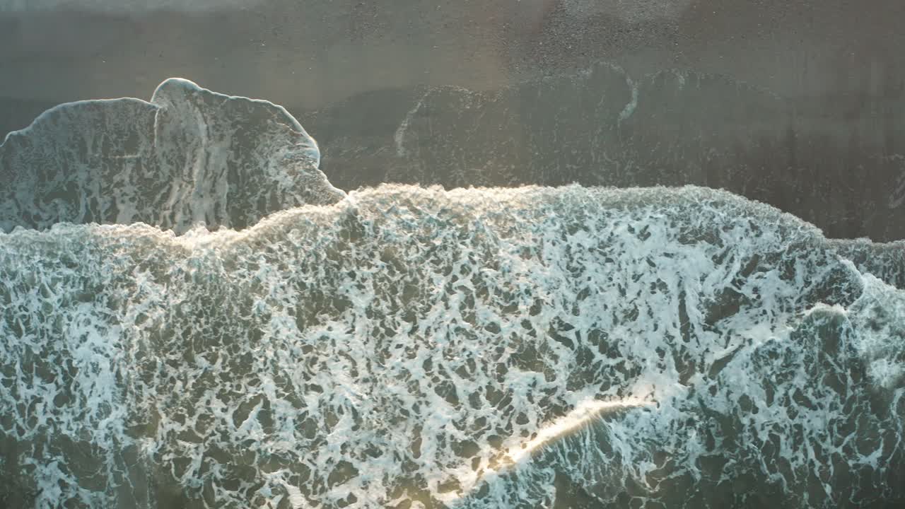 Aerial view over a sandy beach with waves creeping up the screen as the drone slows down