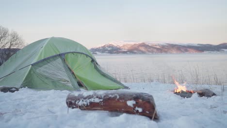 campfire in front of camping tent with lake and mountain views at sunrise