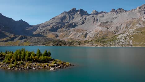 sobrevuelo aéreo a lo largo de una isla en las aguas del lago de salenfe en valais, suiza en un soleado día de otoño en los alpes suizos con picos alpinos y acantilados en la distancia