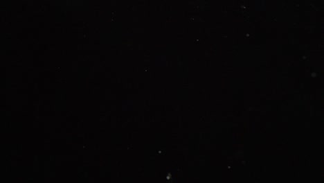 primer plano de hundimiento de gafas rojas cayendo en el agua en tiempo real con superficie negra