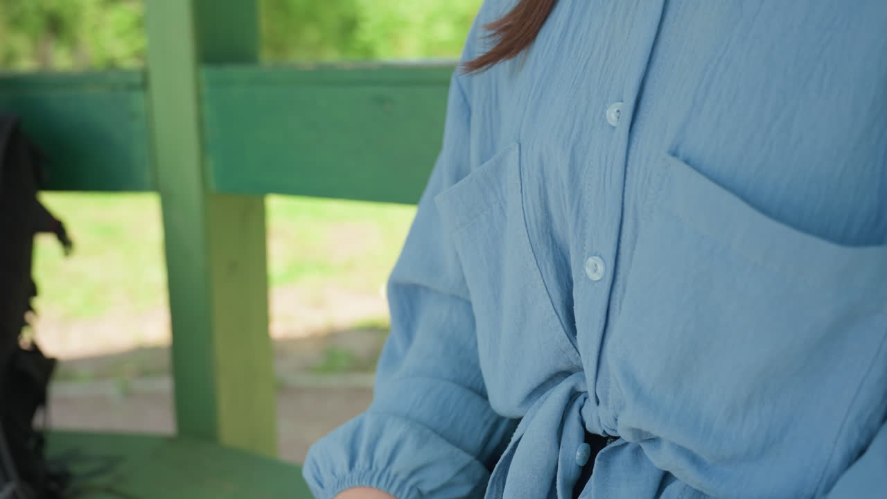 한 여성이 야외에서 화장솜을 사용하고 있어요. 파란색 블라우스를 입은 여성이 밖에서 조심스럽게 위생적인 행동을 하고 있으며, 코카서스 여성이 야외에서 파란색 블라우스를 입은 채 주머니에서 화장솜을 꺼내고 있습니다.