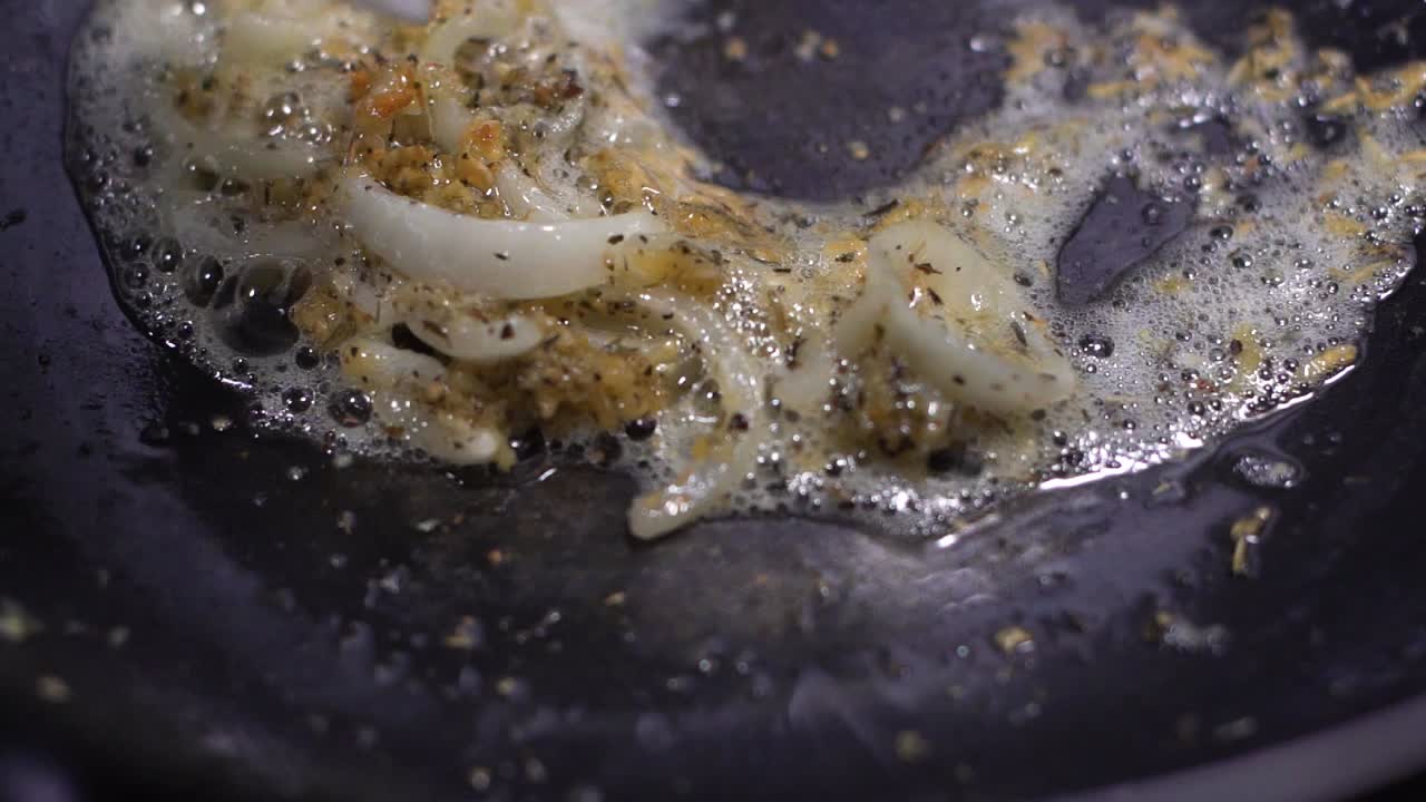 Minced sizzling garlic sauteed with sliced onions in black fry pan with white spatula