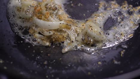 chisporroteante ajo picado salteado con rodajas de cebolla en una sartén negra con una espátula blanca