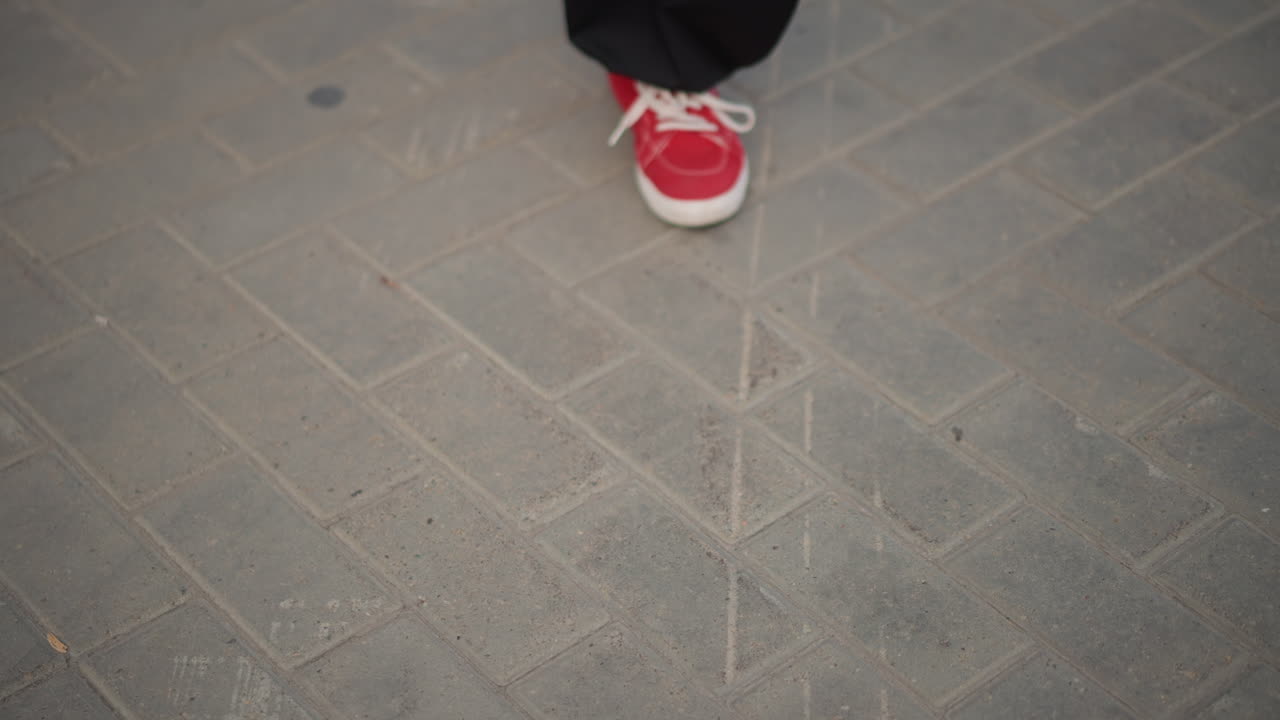 red sneakers on pavement rhythmic footwork captured in closeup. urban dancer practices precise steps and shuffles across textured concrete tiles casual black trousers, laced red footwear, tapping