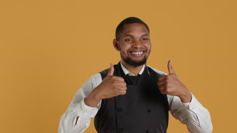 Waiter-smiling-and-showing-a-thumbs-up-symbol-against-yellow-background