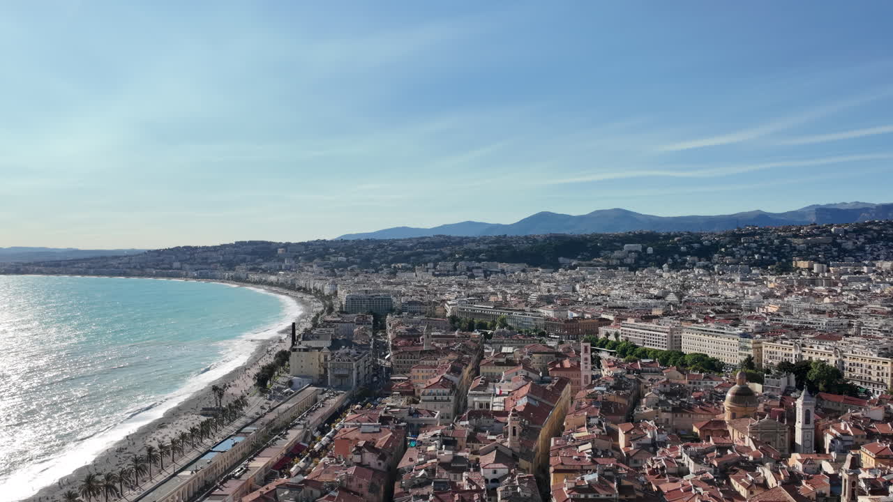 Aerial view of Nice, France with red tiled rooftops, sweeping bay, and mountain backdrop