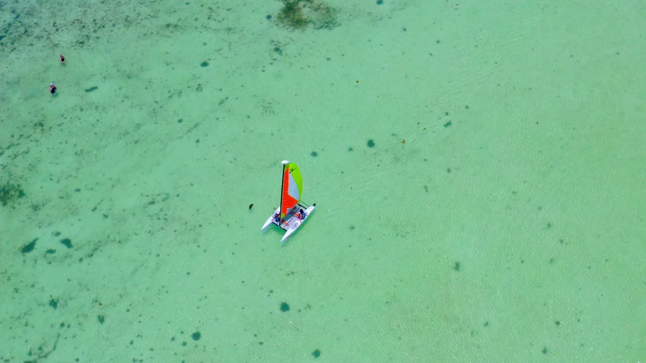 Catamaran with colorful sail navigating on turquoise Caribbean sea water