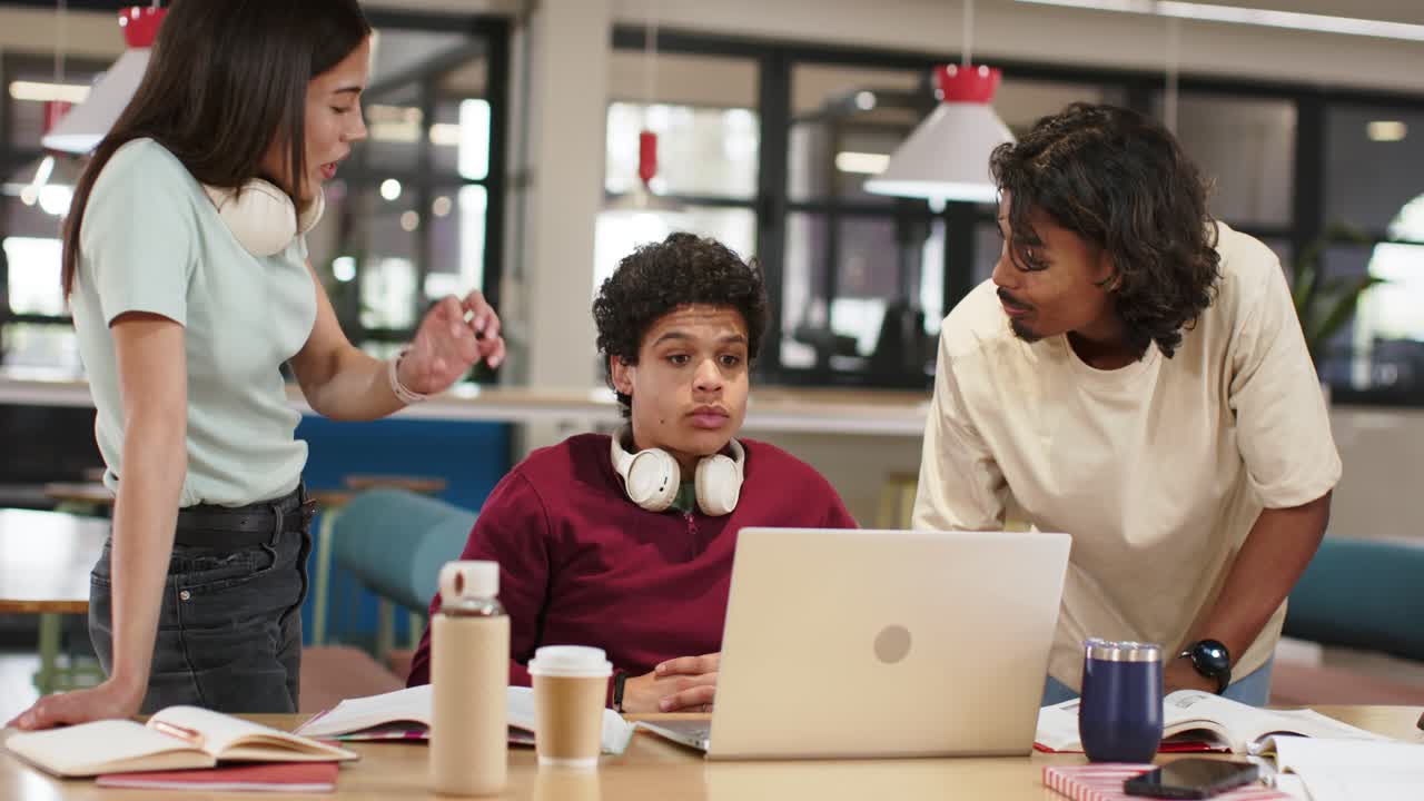 Coworkers at study table, right colleague pointing at laptop, man with headphones reviewing notes