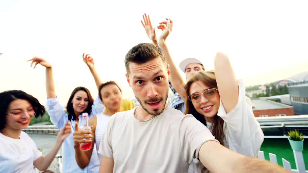 수염이 있는 남자, 인기 있는 블로거가 친구들과 함께 춤추고 웃는 현대적인 야외 파티에서 인터넷 블로그를 위해 비디오를 녹음하는 시점입니다.