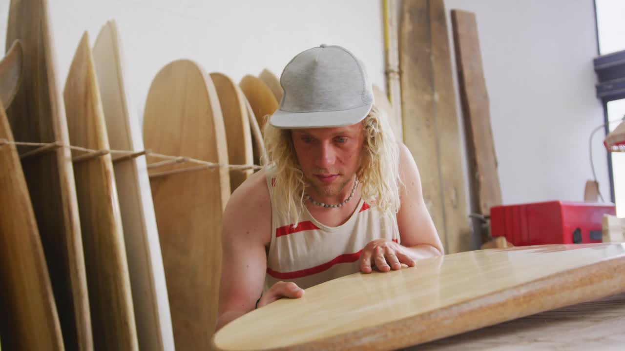 Hvit mannlig surfbrettprodusent sjekker et av surfebrettene i studioet sitt.
