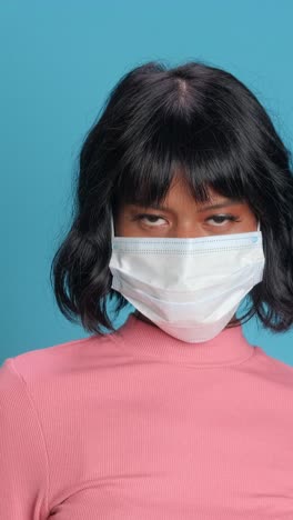 woman in a pink sweater wears a mask against a vibrant blue background