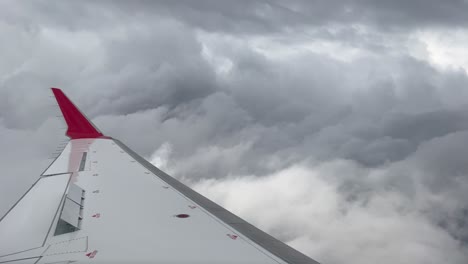 side view of a medium jet plane crossing a turbulent sky plenty of stormy clouds with the airbrakes deployed and a red winlet