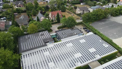 stunning aerial of an industrial buildings roof covered with photovoltaic solar panels on a sunny day. the drone flies backwards and reveals ev's being charged by power generated by the building