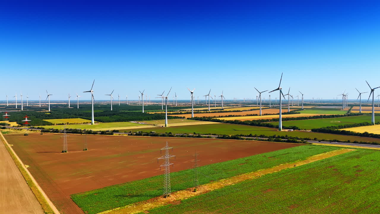 Turbines dot the rolling fields. A landscape features numerous wind turbines operating in a green field under a clear blue sky during daytime