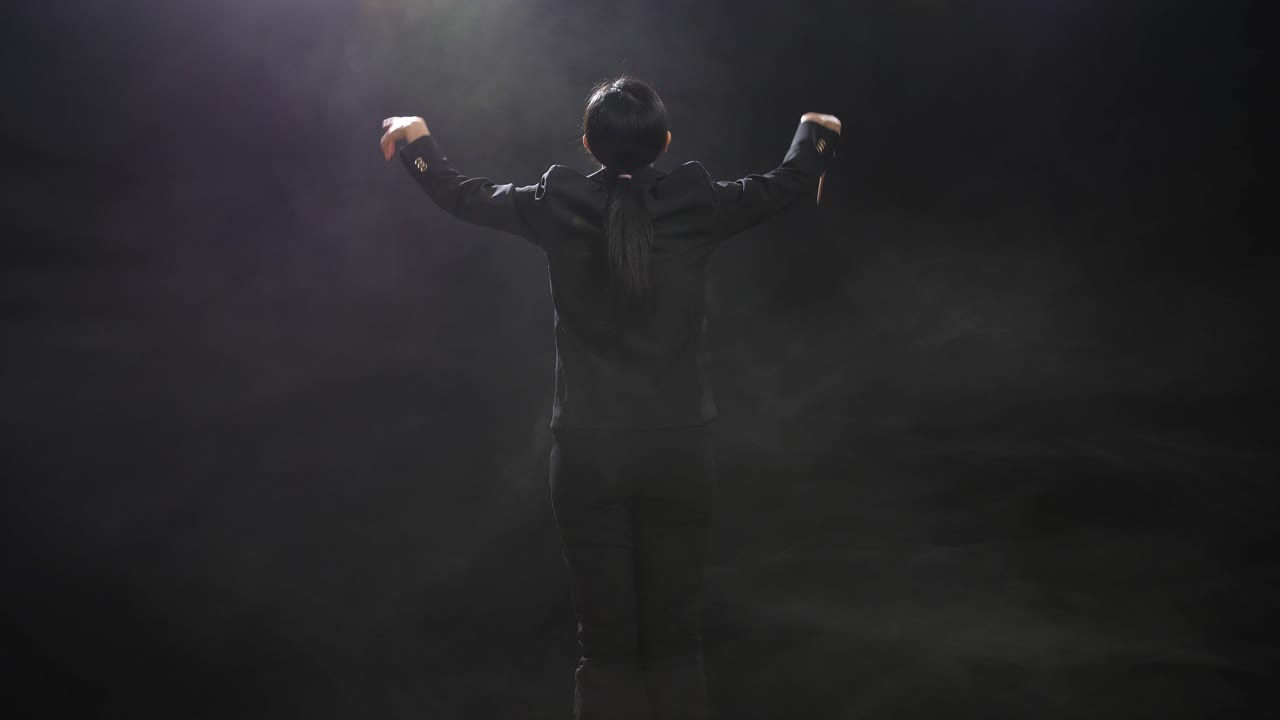 안개가 있는 검은색 스튜디오에서 지이를 들고 몸짓을 하는 아시아계 지휘자 여성의 뒷면