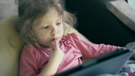 Porträt-Eines-Hübschen-Kleinen-Mädchens,-Das-Auf-Dem-Sofa-Unter-Der-Decke-Liegt-Und-Auf-Einem-Tablet-Computer-Spielt