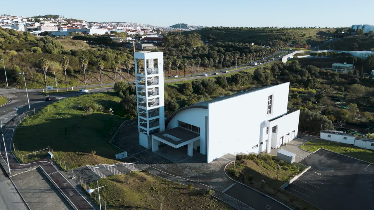 Drone rises up in reverse over Igreja Paroquial de Sao Bras in Amadora Portugal at sunrise, showing the church, surrounding buildings, and urban landscape