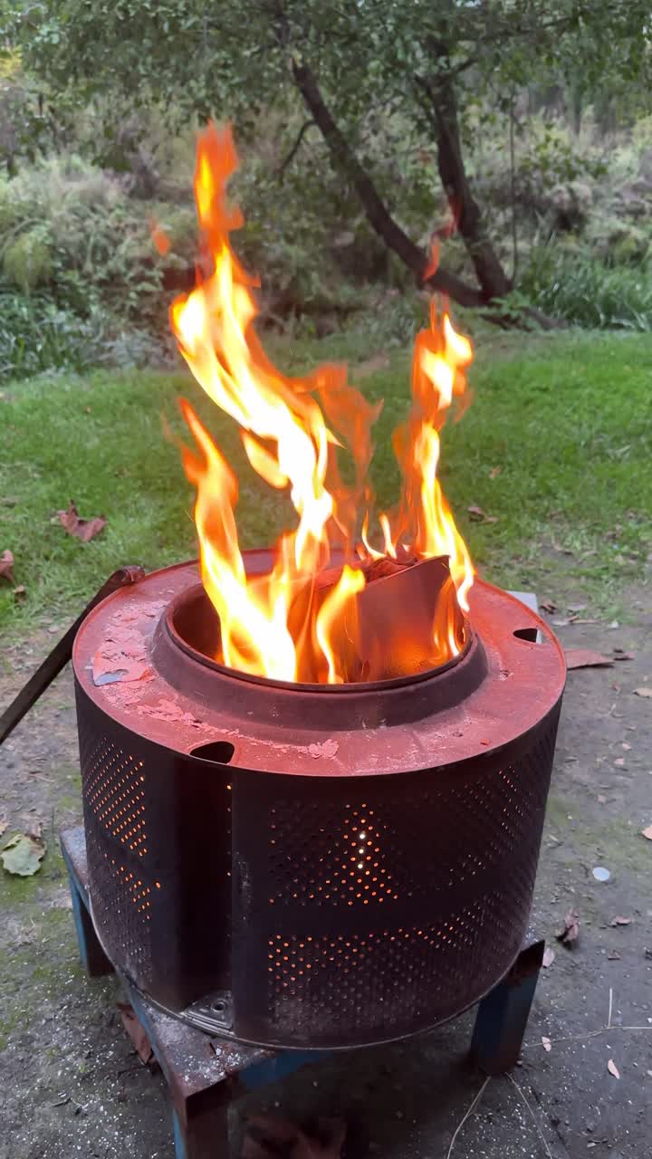 Bright orange flames rising from a metal fire pit outdoors with green grass in background