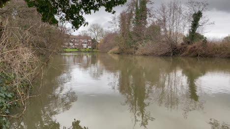 Landschaftsaufnahme-Eines-Trüben-Flusses-Im-Winter-An-Einem-Bewölkten-Tag,-Fluss-Umgeben-Von-Wald