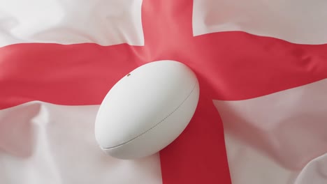 Pelota-De-Rugby-Blanca-Sobre-La-Bandera-Ondeante-De-Inglaterra-Con-Espacio-Para-Copiar,-En-Cámara-Lenta