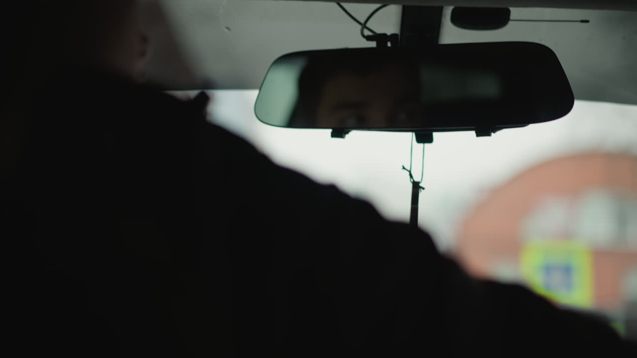 Rear view showing professional driver checking side mirror before turning on busy urban road interior cabin reveals steering wheel in hand concentration on safe maneuver under overcast winter sky