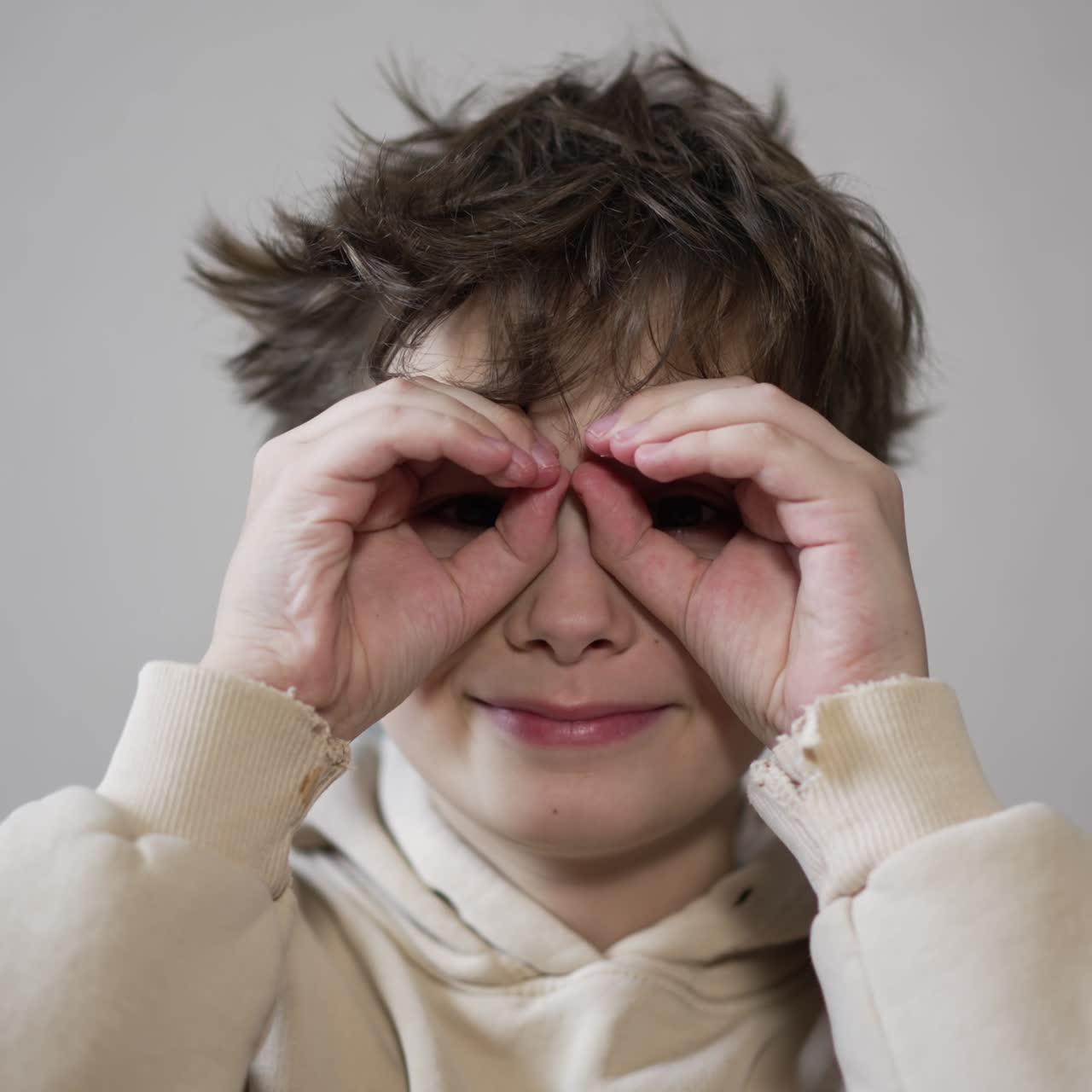 Portrait of a nice smiling kid looking into camera. Boy puts his hands on face making glasses and turns to the sides. Close up