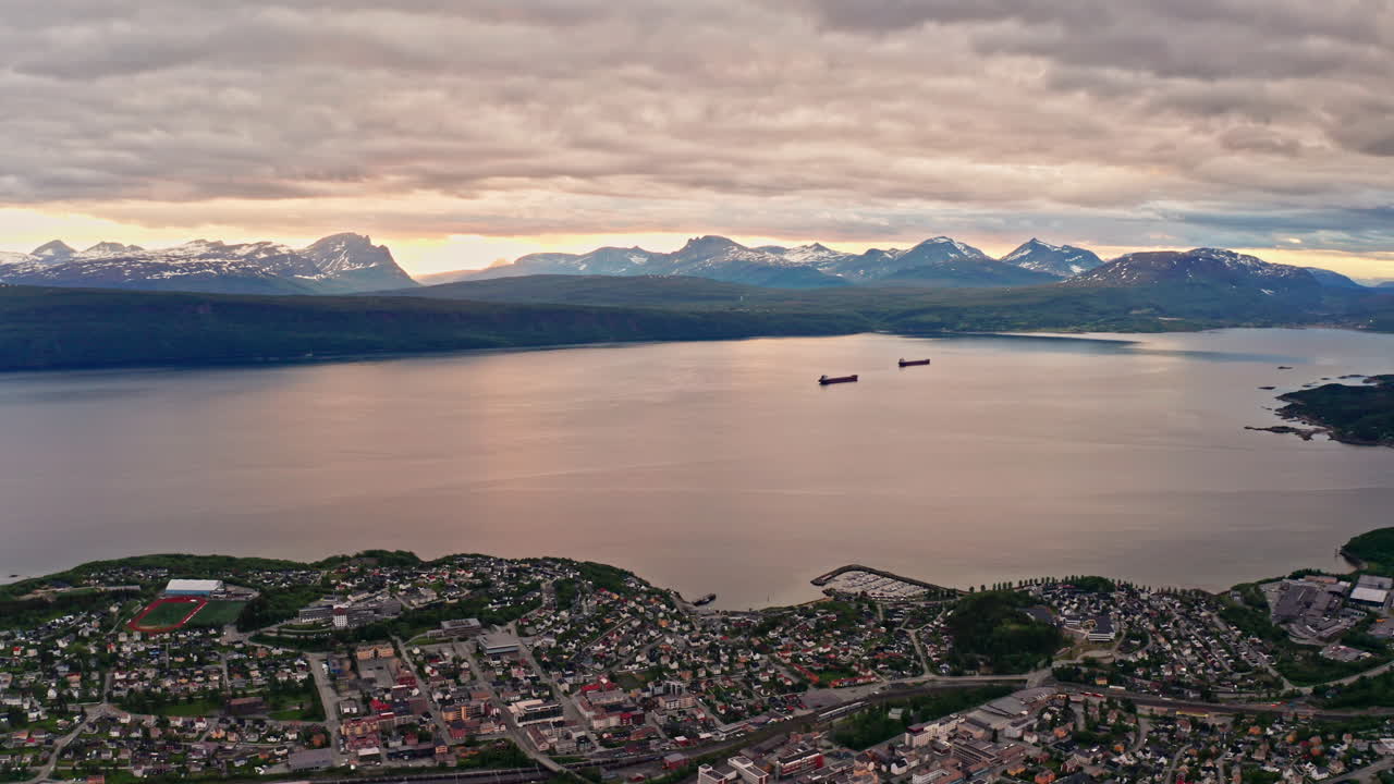 Aerial drone shot over the city of Narvik in Norway at sunset. High view of the nordic city located at the coastline. View of the sea and the mountains in the distance.