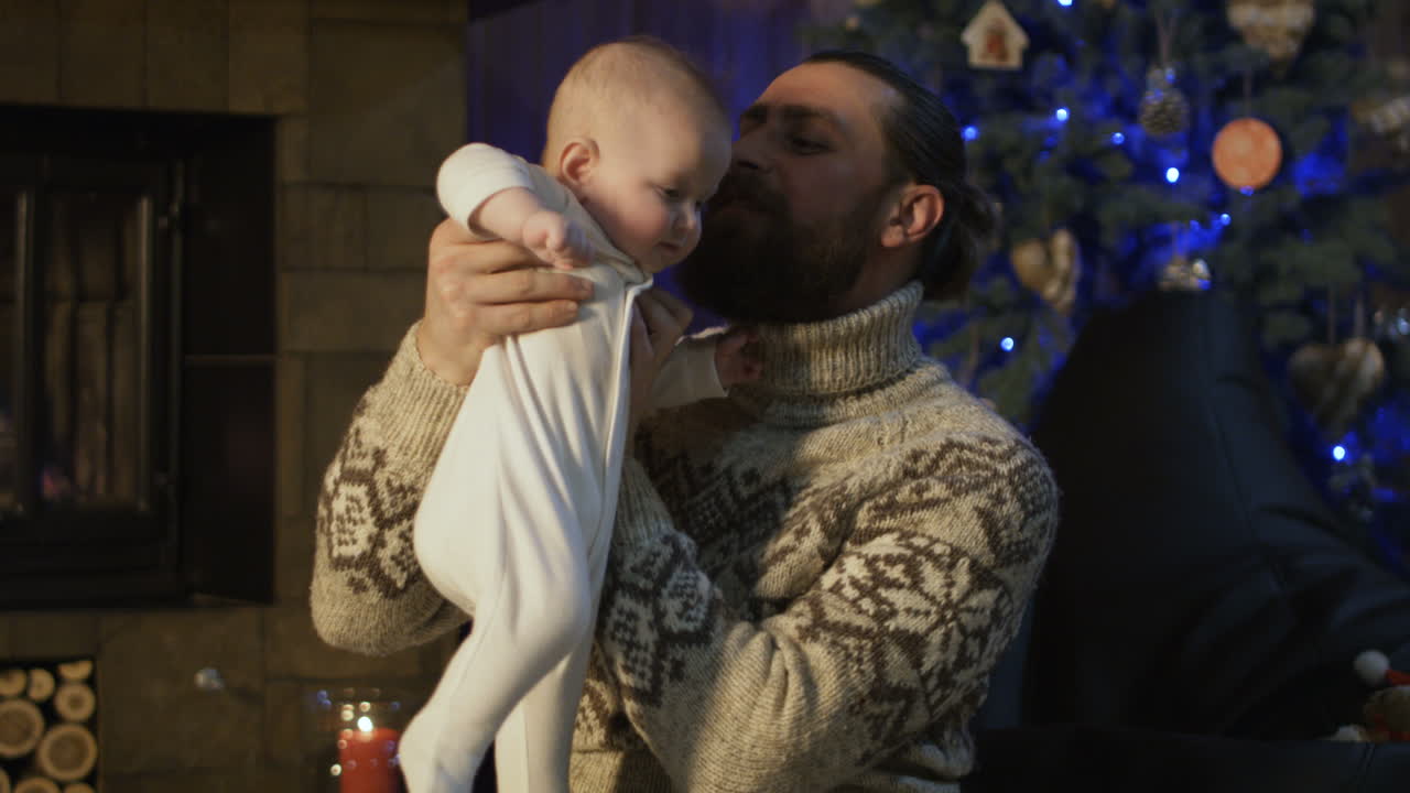 Father holding baby by fireplace during Christmas