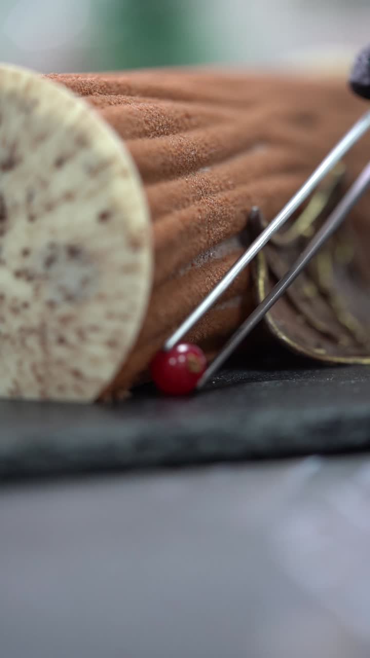 Uno chef decora un tronchetto di cioccolato con ciliegia, copertura al cacao texturizzata e dettagli decorativi a forma di foglia, inquadratura ravvicinata, inquadratura di dettaglio
