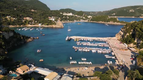 Aerial-pullback-above-bustling-harbor-and-sandy-beach-in-Corfu-Greece-with-coastal-view-homes-and-shops