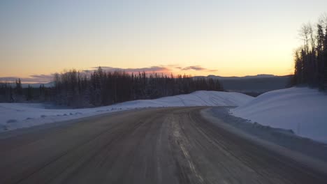 pov shot driving on slippery road, in middle of frosty forest and arctic nature, at dusk, in yukon, canada