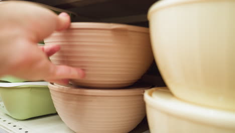 view of a hand placing a bowl in the bowl section of a store. the scene features various bowls, including green and brown ones, neatly arranged on shelves