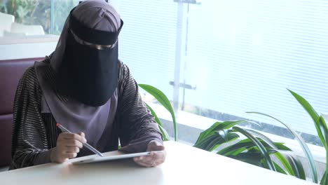 mujer musulmana en niqab usando una tableta en un café