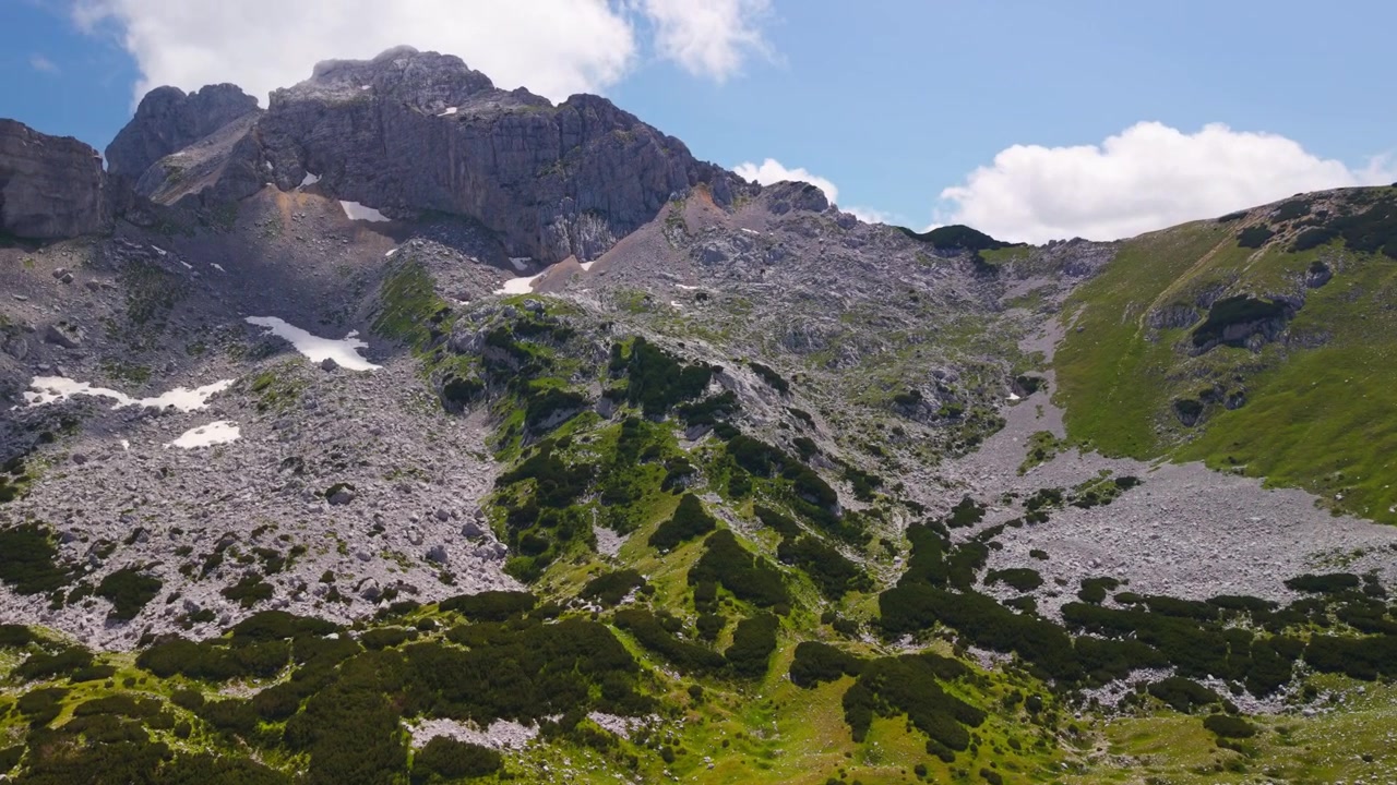 Højt luftfoto af en grøn alpedal omgivet af klippetoppe og lave skyer i Durmitor Nationalpark, Montenegro
