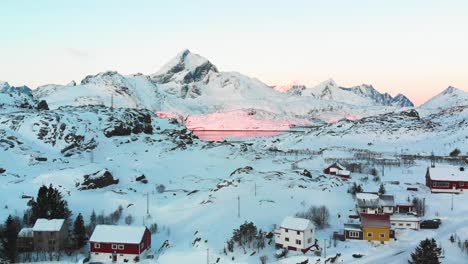 Drohnenblick-Auf-Eine-Kleine-Stadt-Im-Winter-Auf-Den-Lofoten-Und-Den-Sonnenaufgang-Im-Fjord-Im-Hintergrund-Mit-Den-Bergen