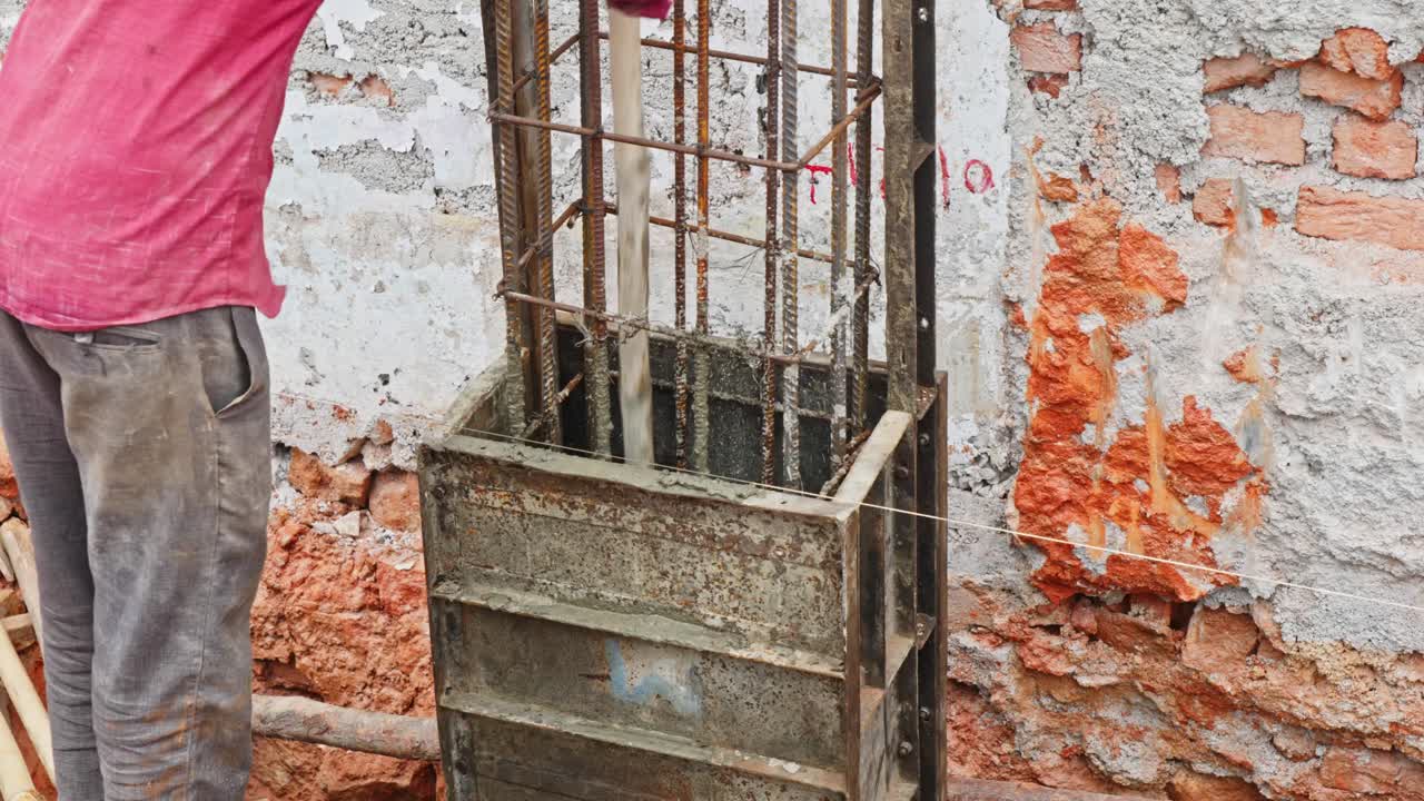 Worker levels concrete inside a steel column framework through wood stick at construction area. day time, stable shot, 4k