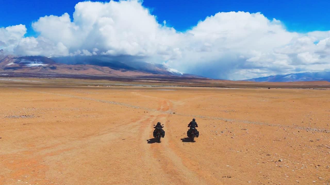 couple of friend adventure motorcycle rider on the red sand desert with snow capped mountains at distance during off road trip