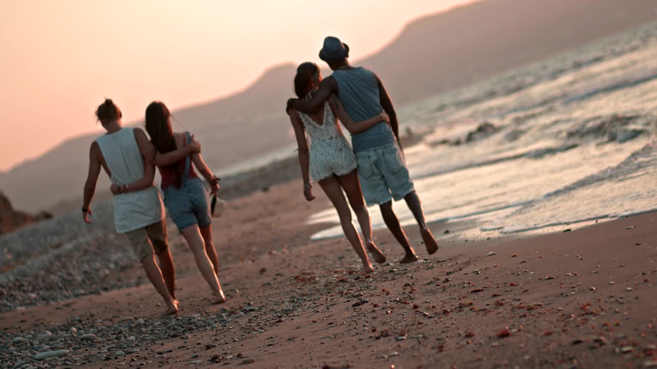 románticas parejas de hipsters multiétnicos caminando por la playa al atardecer