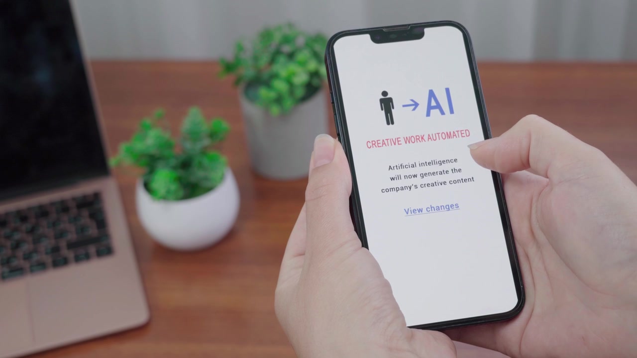 Mani che tengono uno smartphone che mostra un avviso informativo di intelligenza artificiale (AI) che il lavoro creativo dell'azienda sarà ora automatizzato.