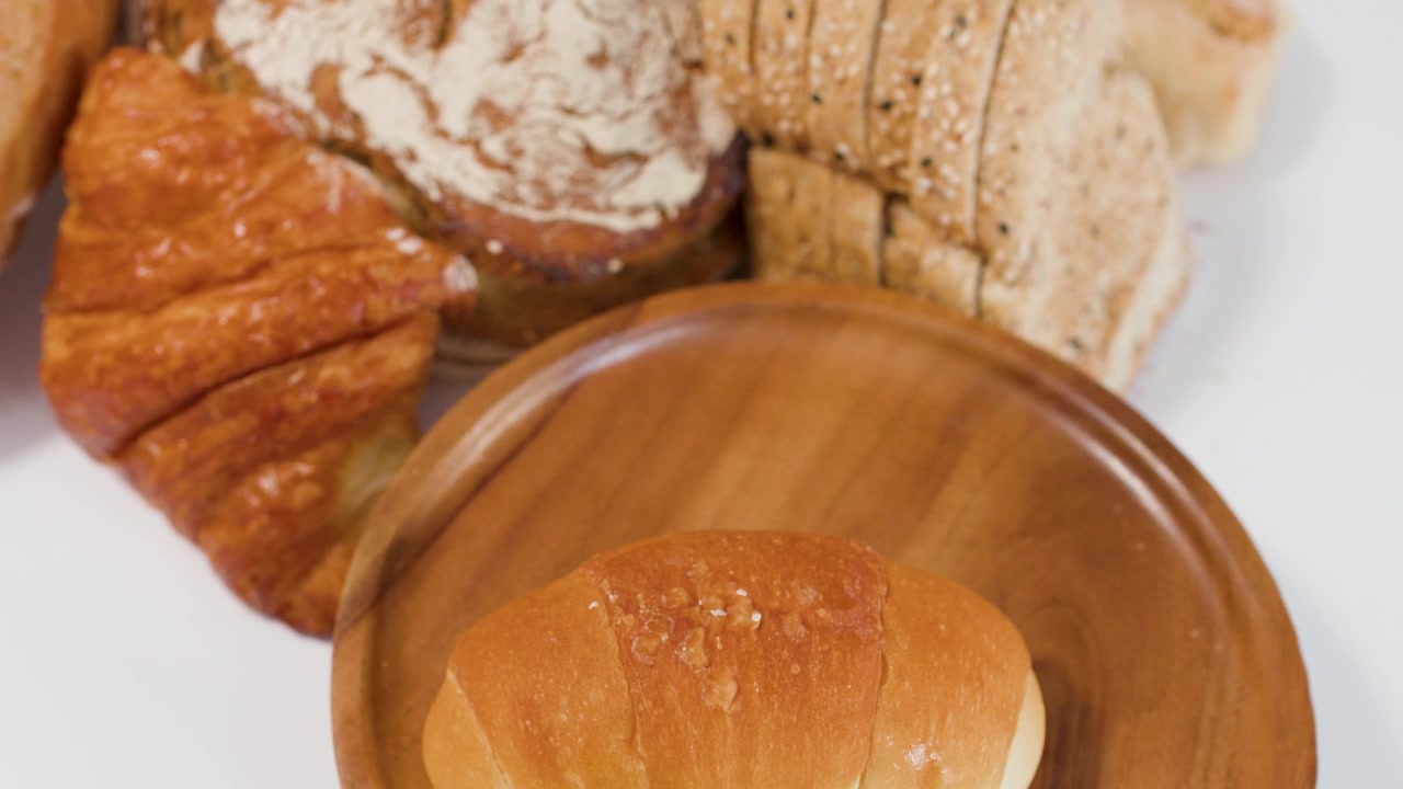 A person places golden bread rolls onto a wooden plate against a white background.